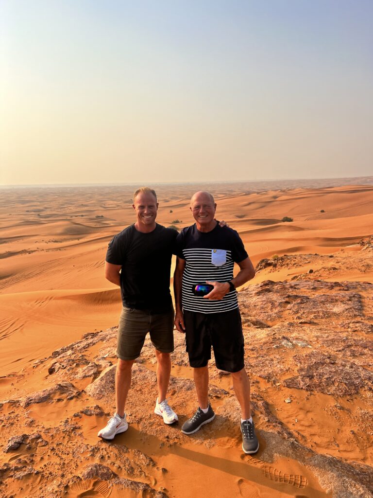 Two men standing arm in arm on a red sand dune in the desert